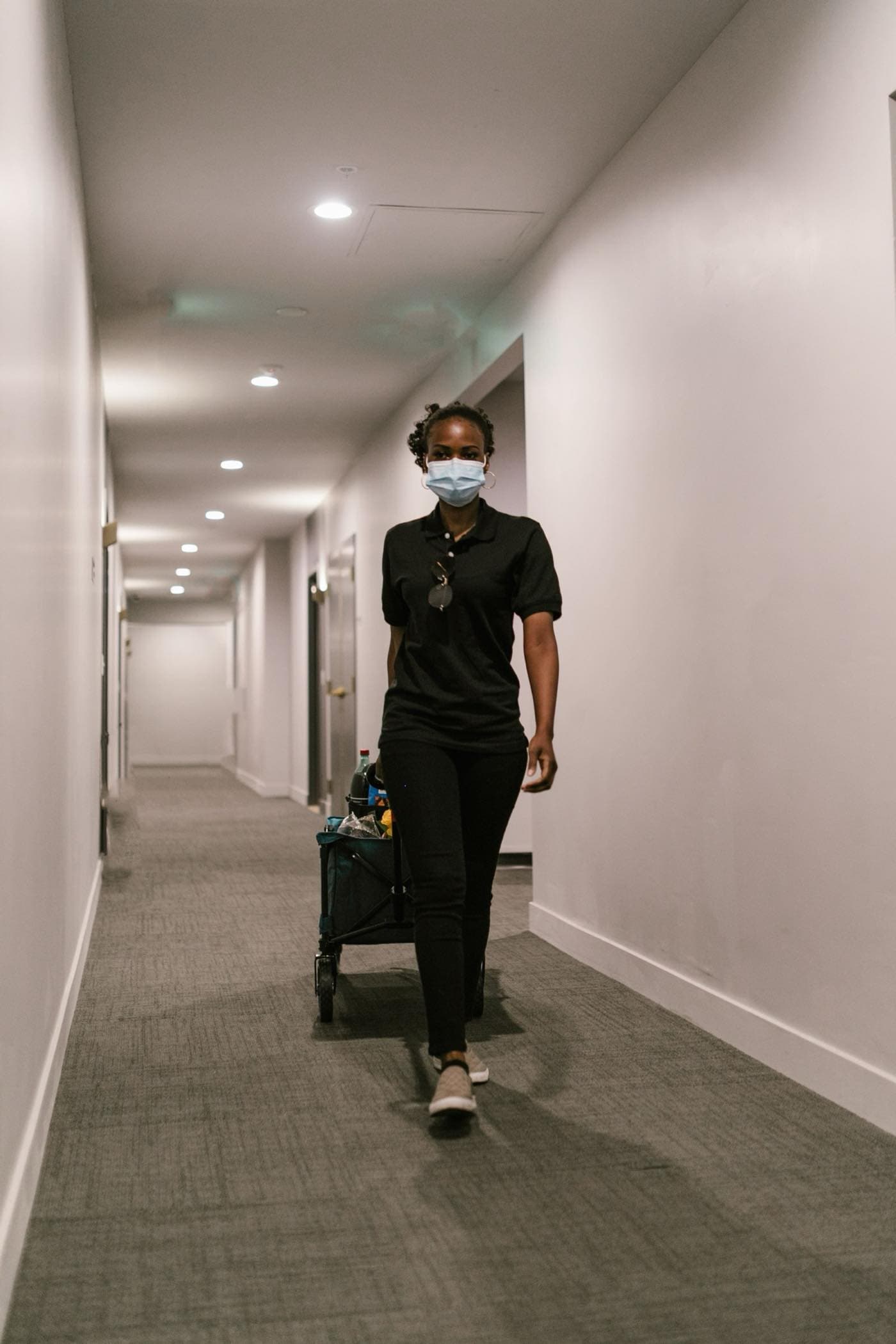 A uniformed janitor walking a corridor with a cleaning cart