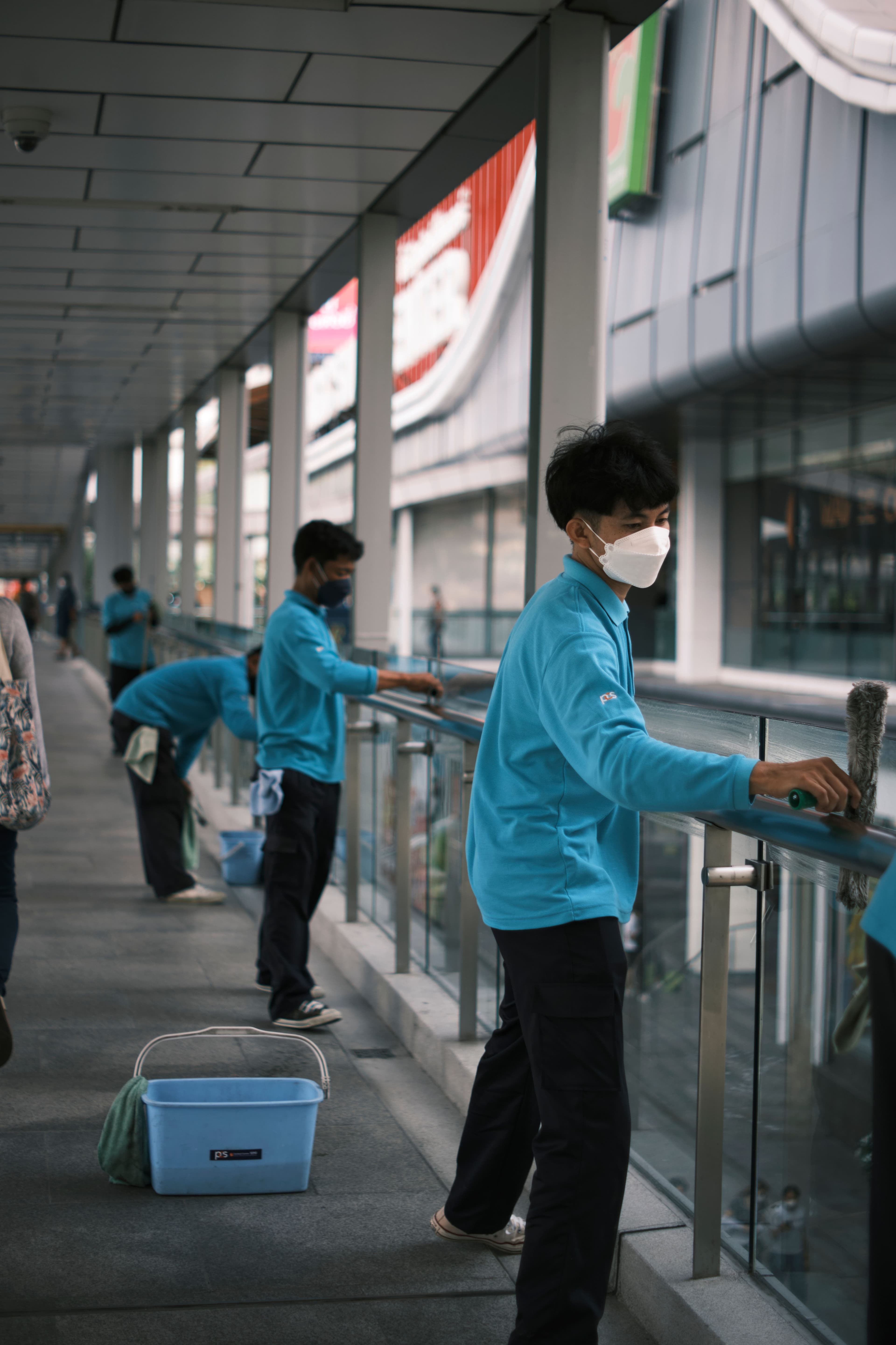A uniformed cleaning crew wiping down glass railings along a commercial walkway
